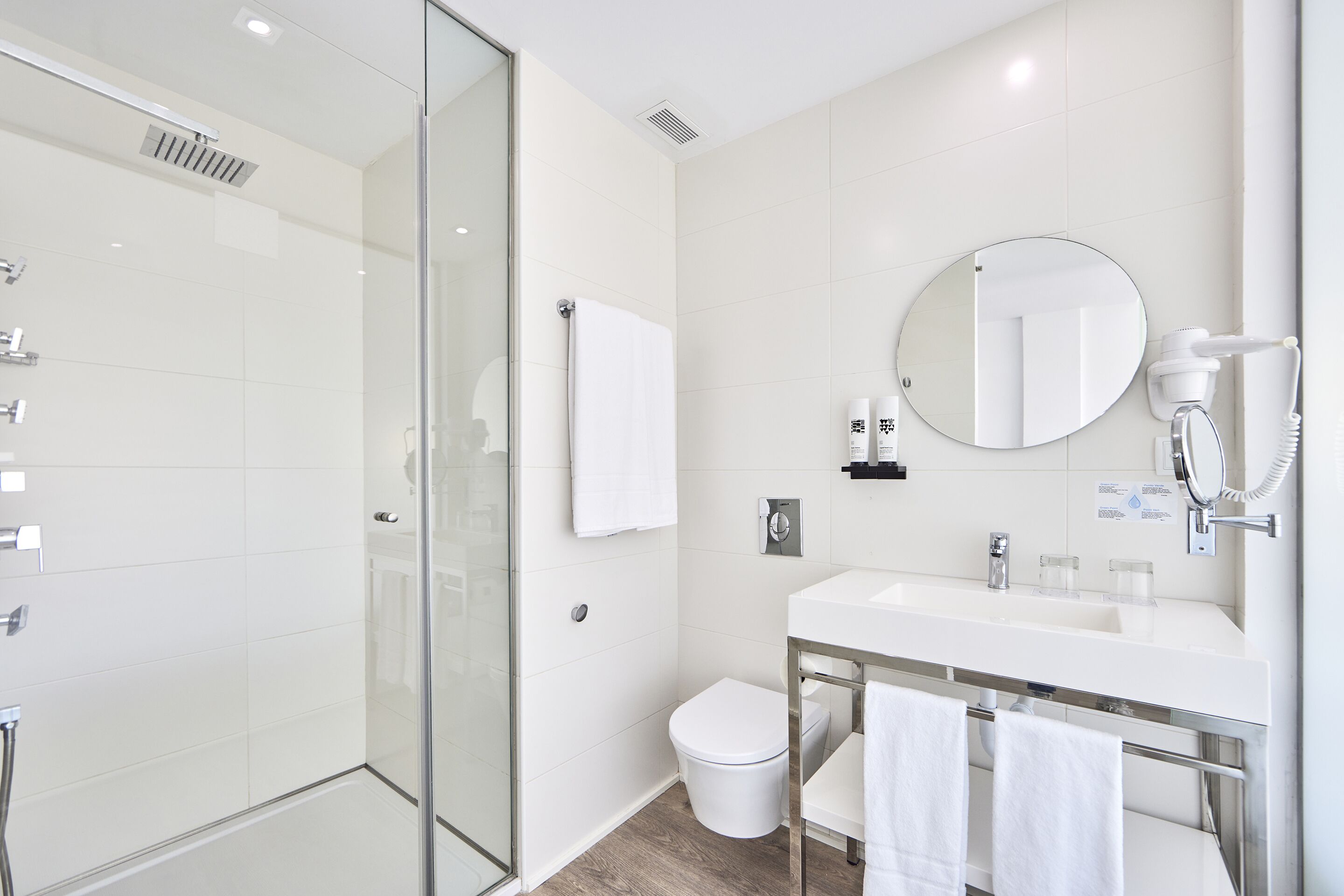 Un baño moderno con cabina de ducha de vidrio, inodoro blanco y tocador con espejo y toallero.