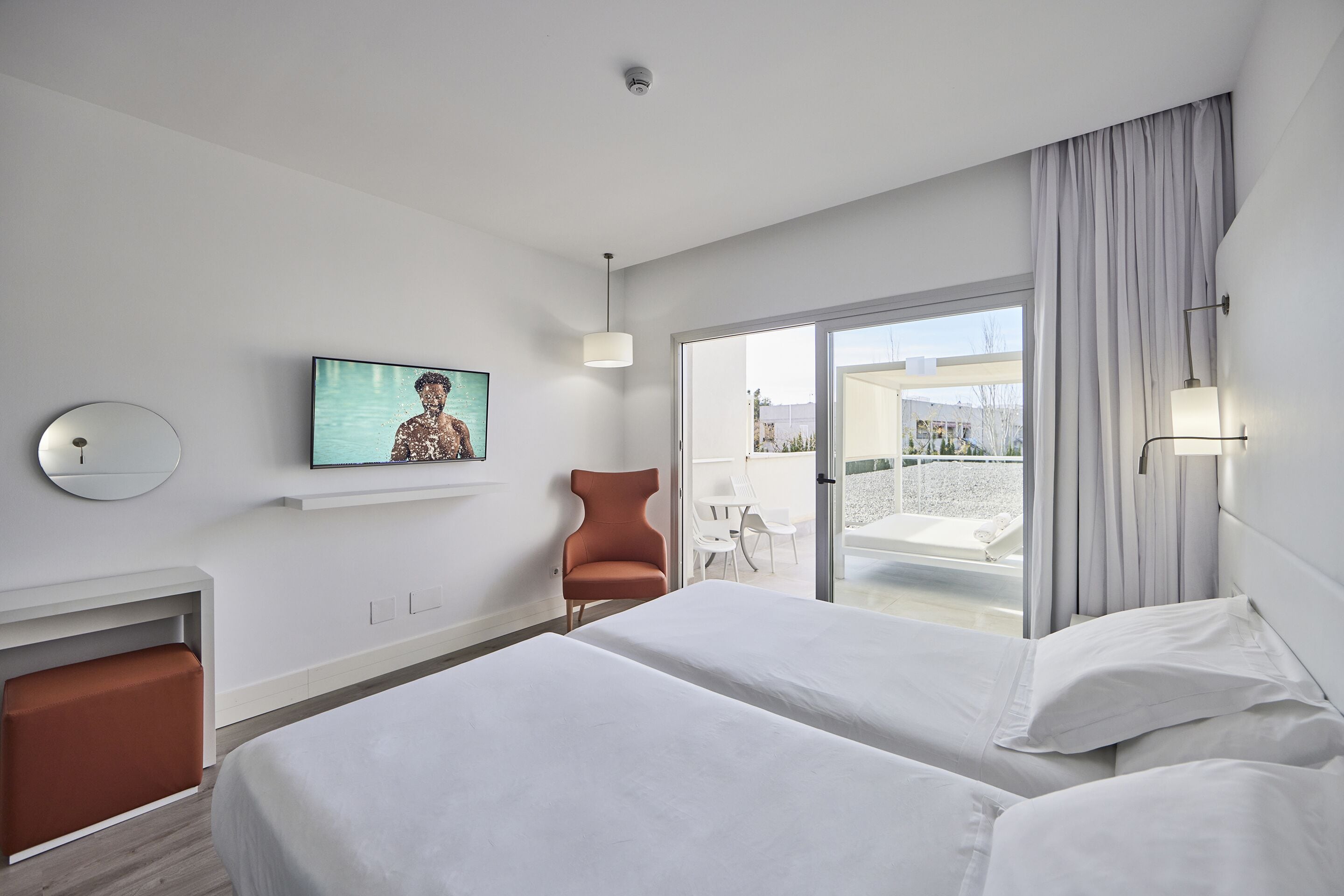 A hotel room with two beds, a TV on the wall, a chair, and a balcony with a view.