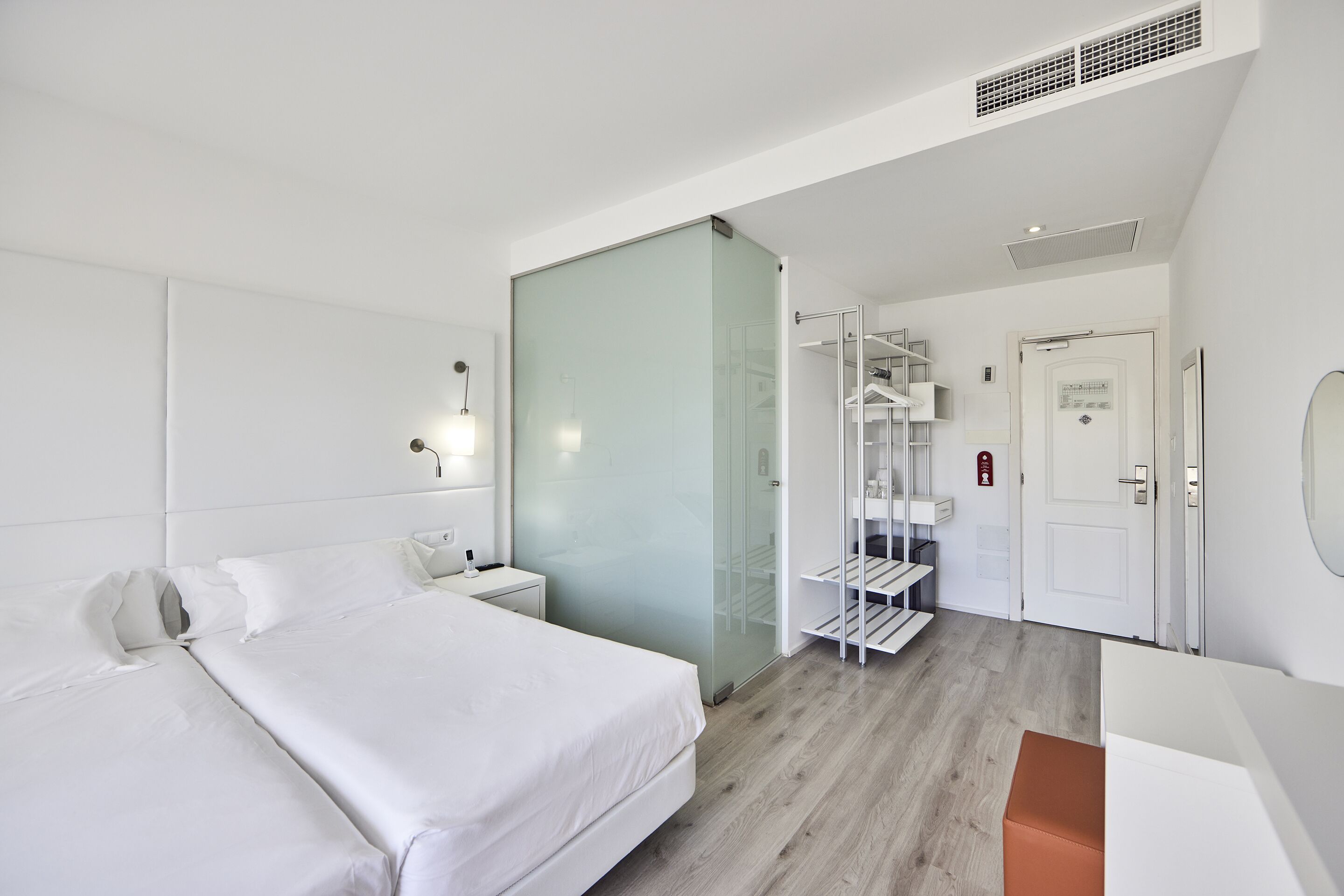 Moderni hotellihuone, jossa on suuri sänky, lasiseinä, sisäänrakennettu vaatekaappi ja pieni oleskelualue.