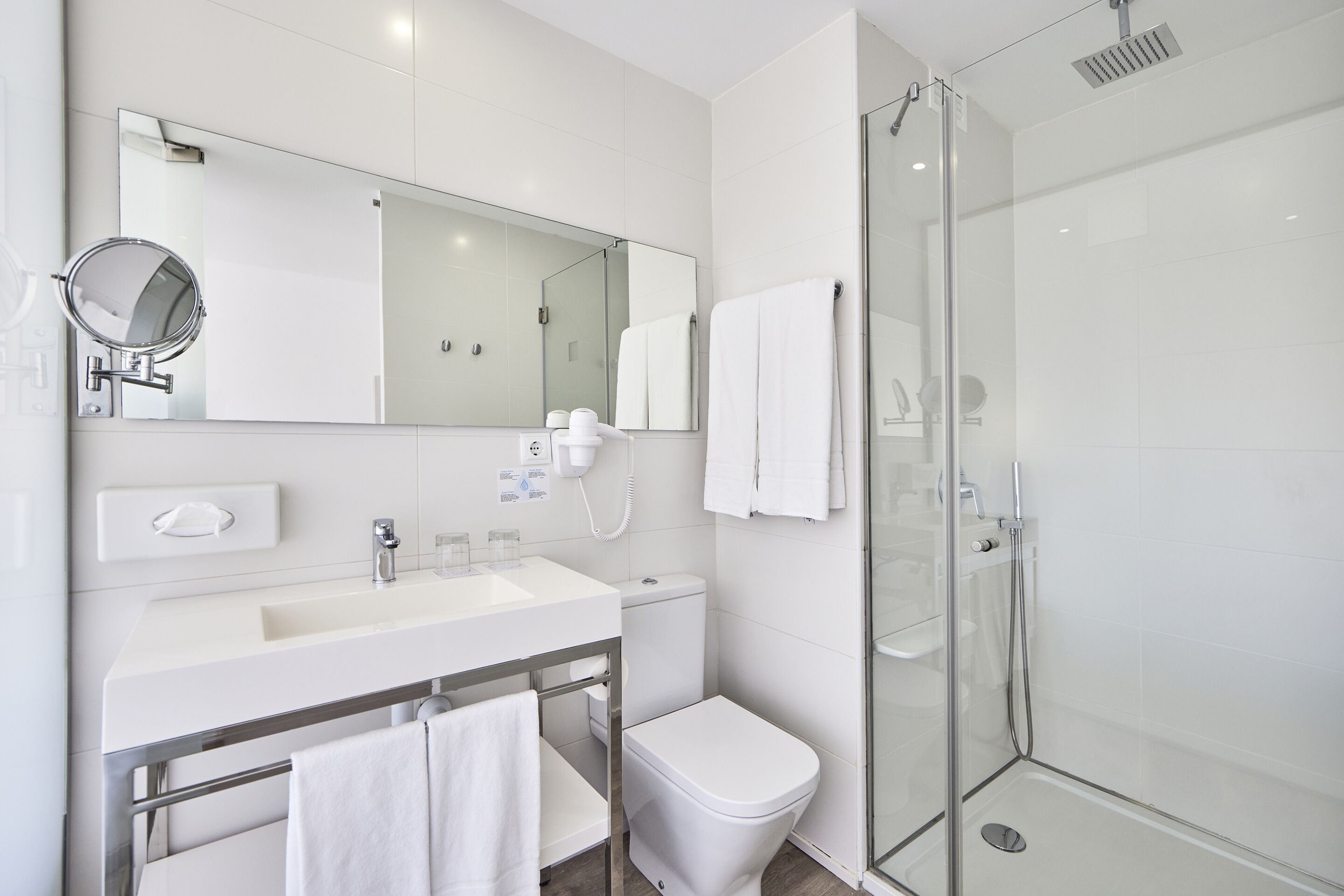Un baño moderno con ducha de vidrio, lavamanos blanco y un espejo grande.