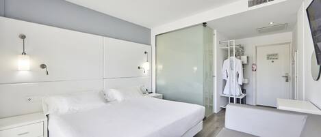 A modern hotel bedroom with a large bed, bedside tables, a wardrobe, and a glass partition.