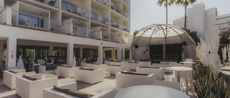 Vestíbulo de hotel con asientos al aire libre, un escenario y palmeras.