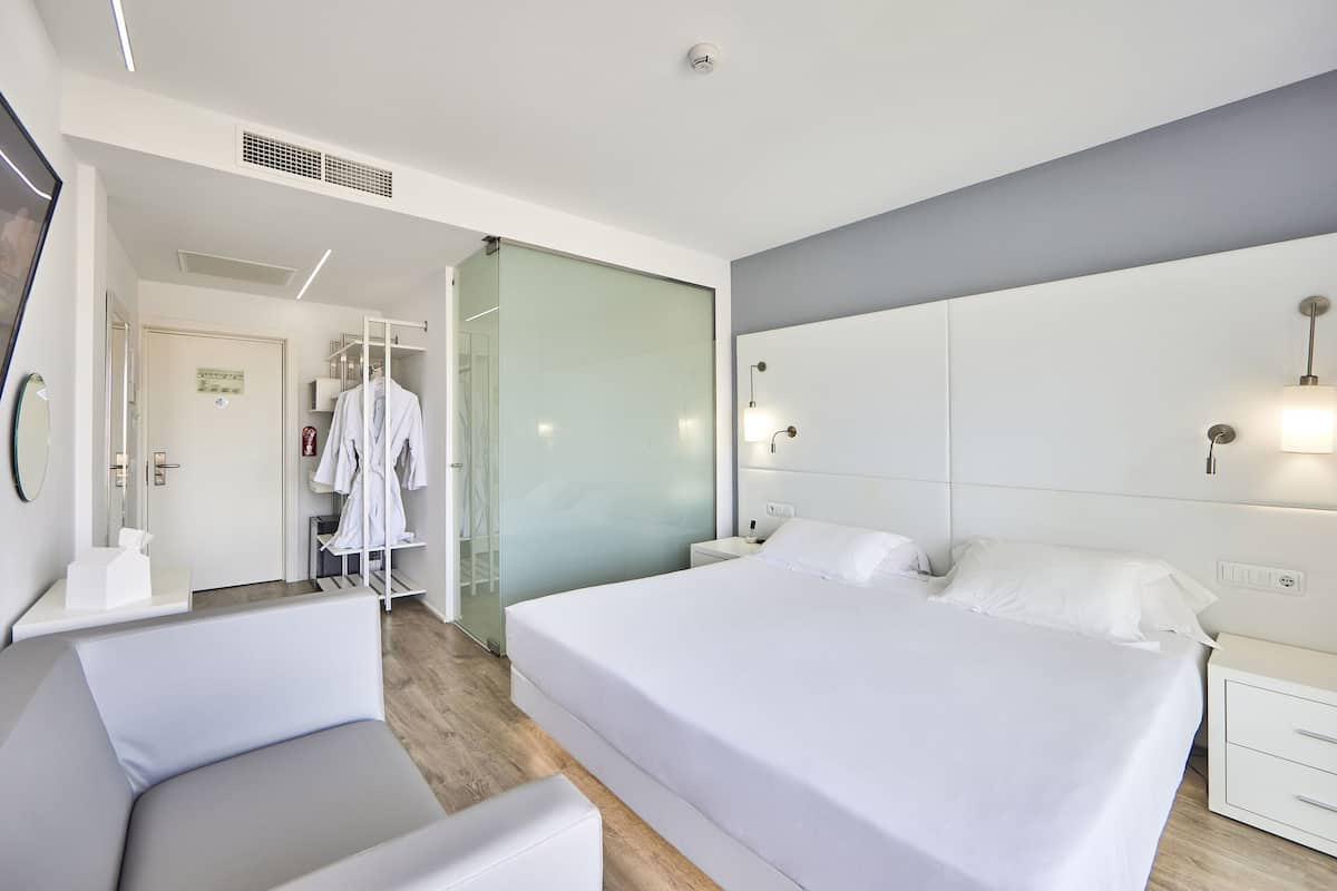 Une chambre d’hôtel moderne avec un grand lit, une table de chevet, une chaise et un dressing.