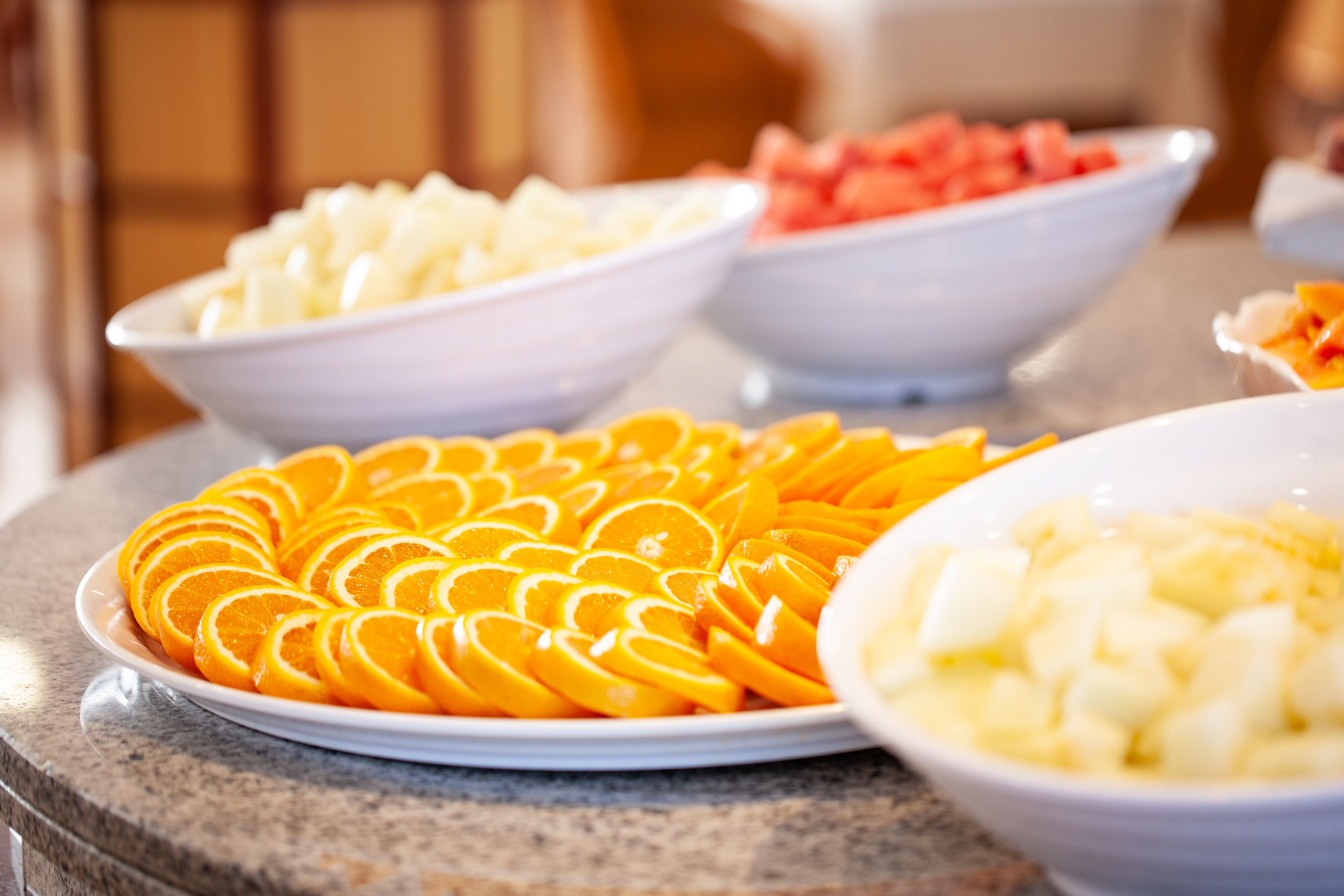 A buffet table with various fruits including oranges, apples, and watermelon.