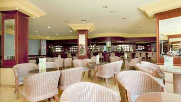 A spacious restaurant with wicker chairs and tables, a bar area, and a view through large windows.