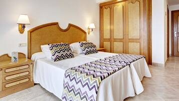 Una habitación de hotel con una cama grande, cabecera de madera, dos mesitas de noche y un armario.