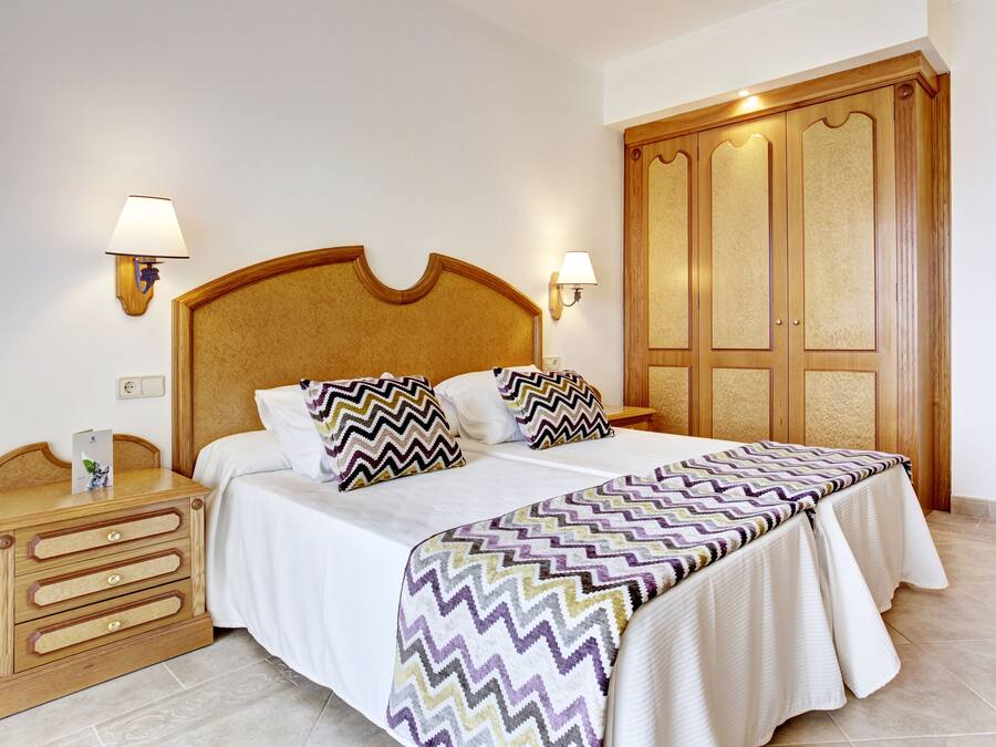 Una habitación de hotel con una cama grande, cabecera de madera, dos mesitas de noche y un armario.