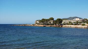 Un hotel frente al mar con varias construcciones, un litoral rocoso y un mar azul cristalino.
