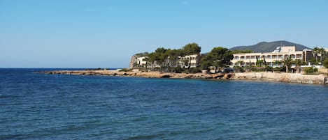 A coastal hotel with multiple buildings, a rocky shoreline, and a clear blue sea.