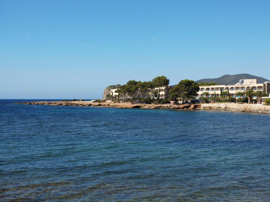 Un hotel frente al mar con varias construcciones, un litoral rocoso y un mar azul cristalino.