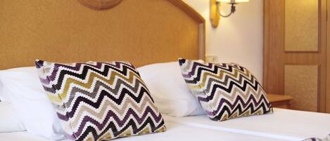 A neatly made bed with two patterned pillows and a wall-mounted lamp.