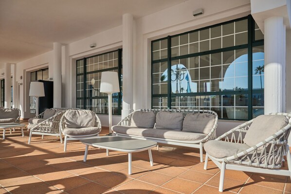 A sunlit outdoor seating area with wicker furniture and large windows. - Grupotel Mar de Menorca (Mahón)