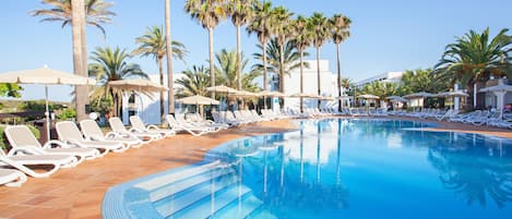 Zona de piscina con tumbonas y sombrillas, rodeada de palmeras.