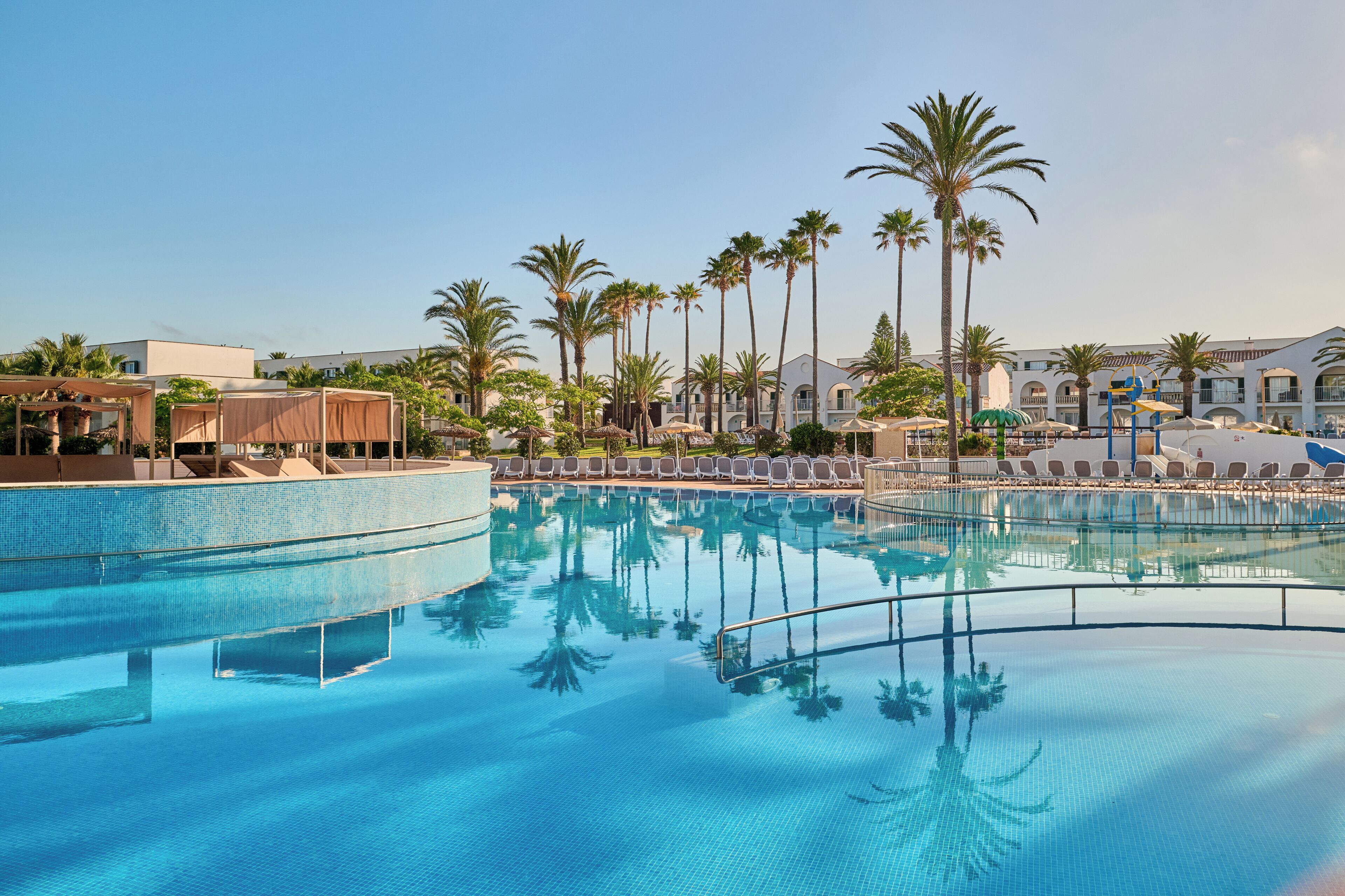 Une piscine à l’eau d’un bleu cristallin, entourée de chaises longues et de palmiers.