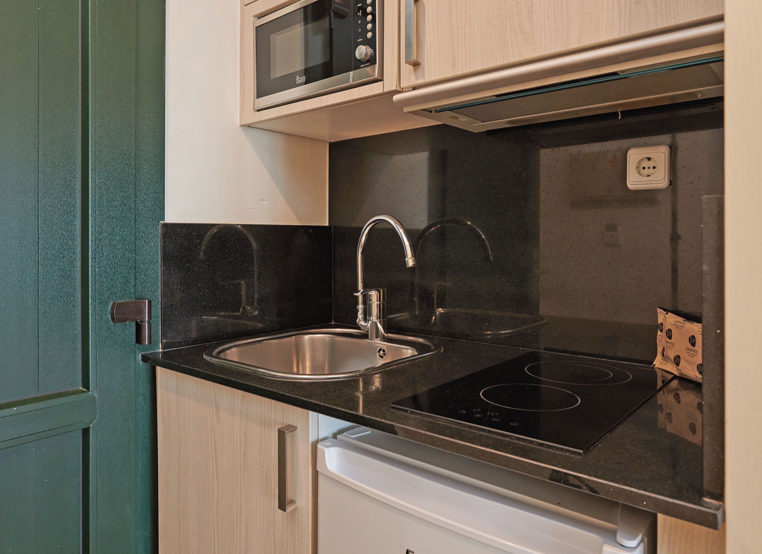 Een kleine keuken met een magnetron, spoelbak en fornuis.