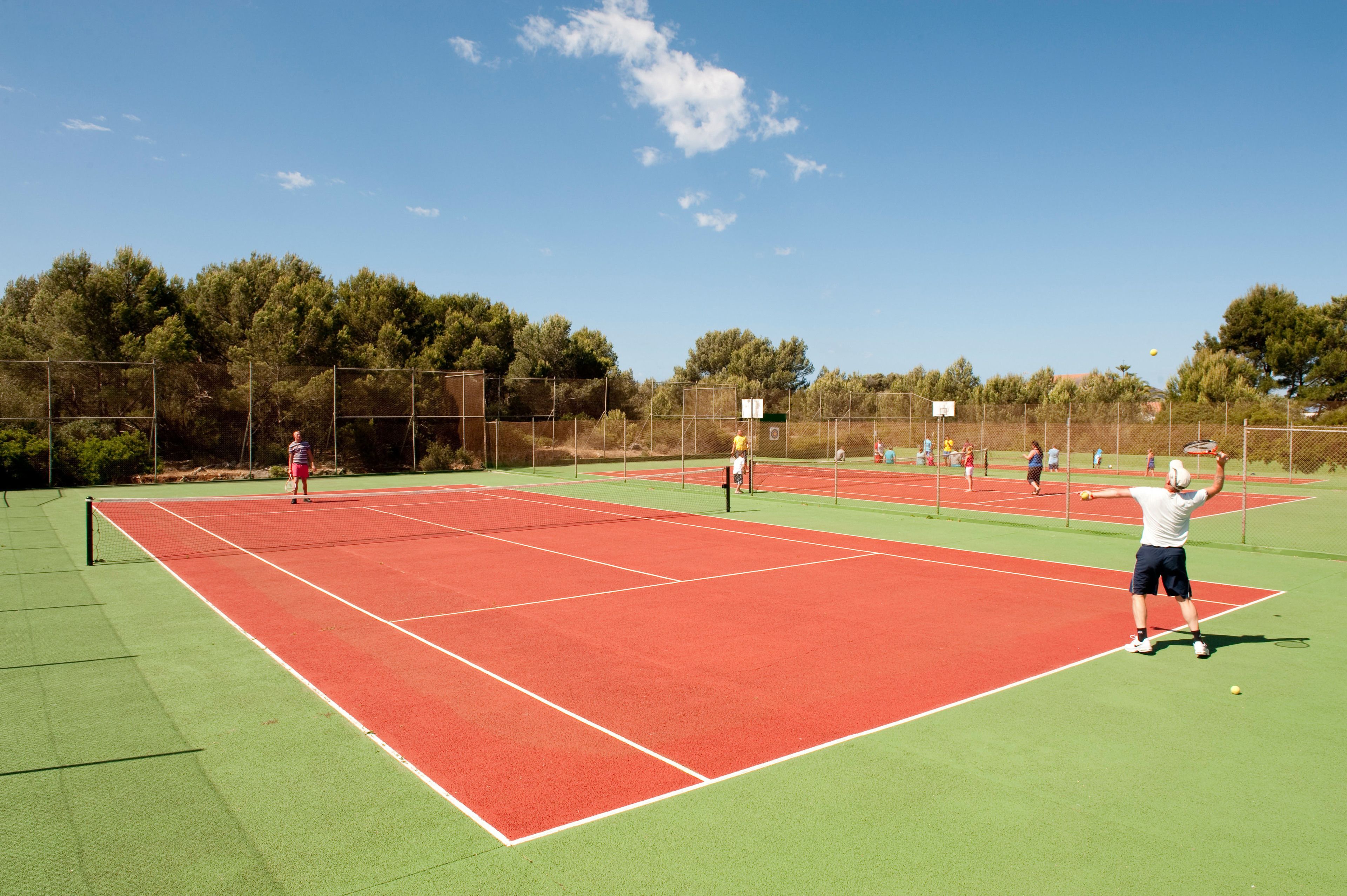 Una cancha de tenis al aire libre con varios jugadores.