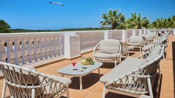 Una terraza con mobiliario de mimbre, una mesa con bebidas y vista al mar.