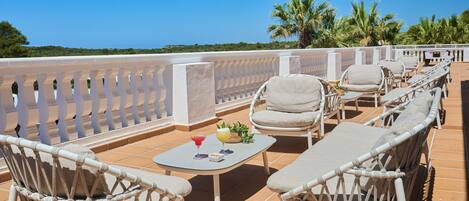 Una terraza con mobiliario de mimbre, una mesa con bebidas y vista al mar.