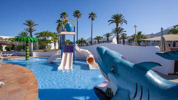 A pool area with a shark slide and a water play structure.