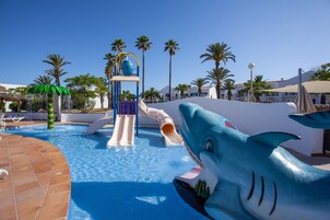 Un área de piscina con un tobogán con forma de tiburón y una estructura de juegos acuáticos.