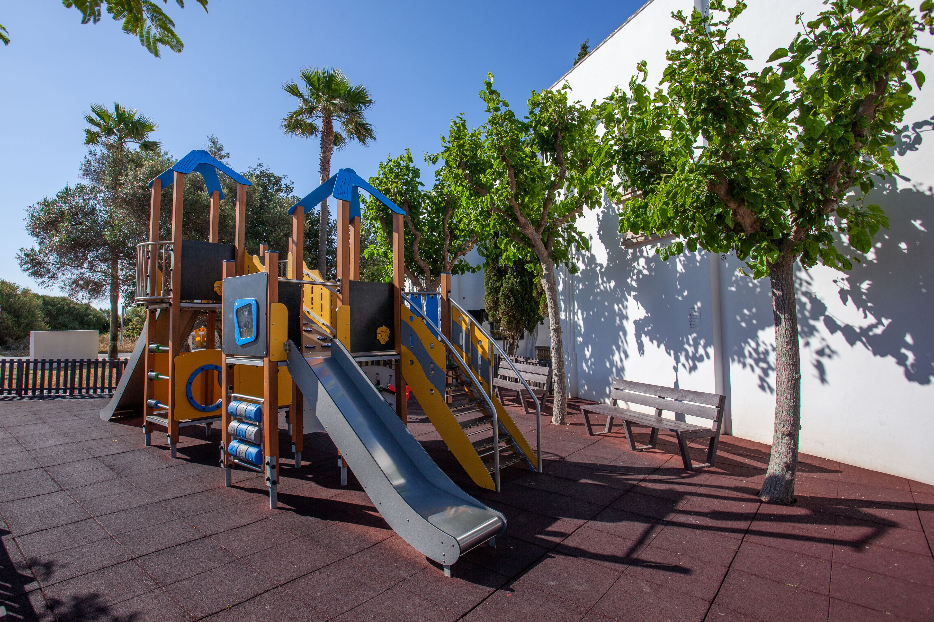 A playground with slides and climbing structures, a bench, and a tree.