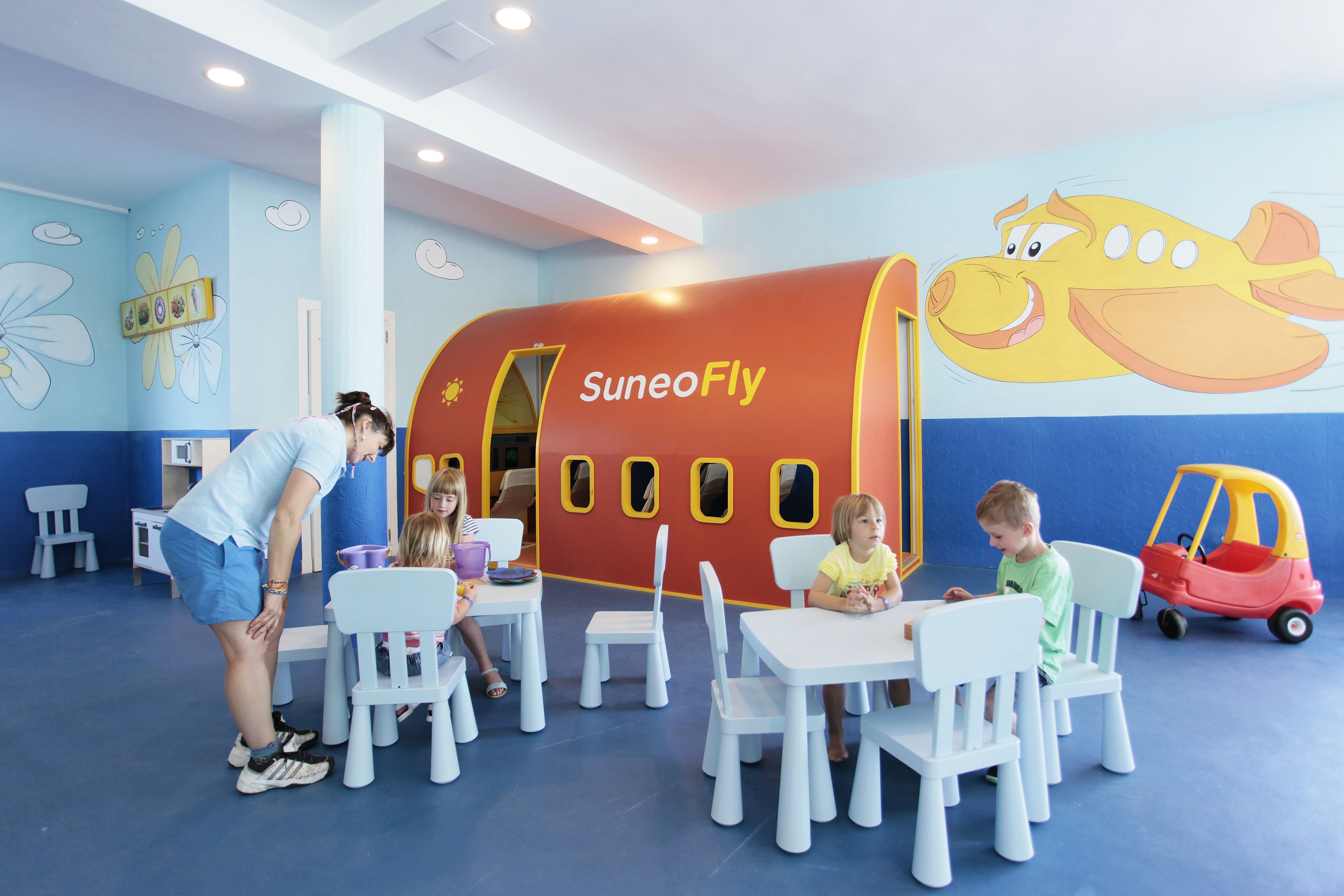 A children's play area with a large mural of a flying airplane and a small toy car.
