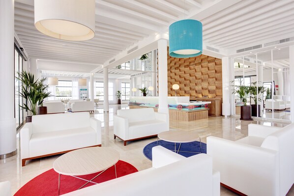 A spacious lobby with white sofas, a reception desk, and a wooden wall. - Grupotel Mar de Menorca (Mahón)