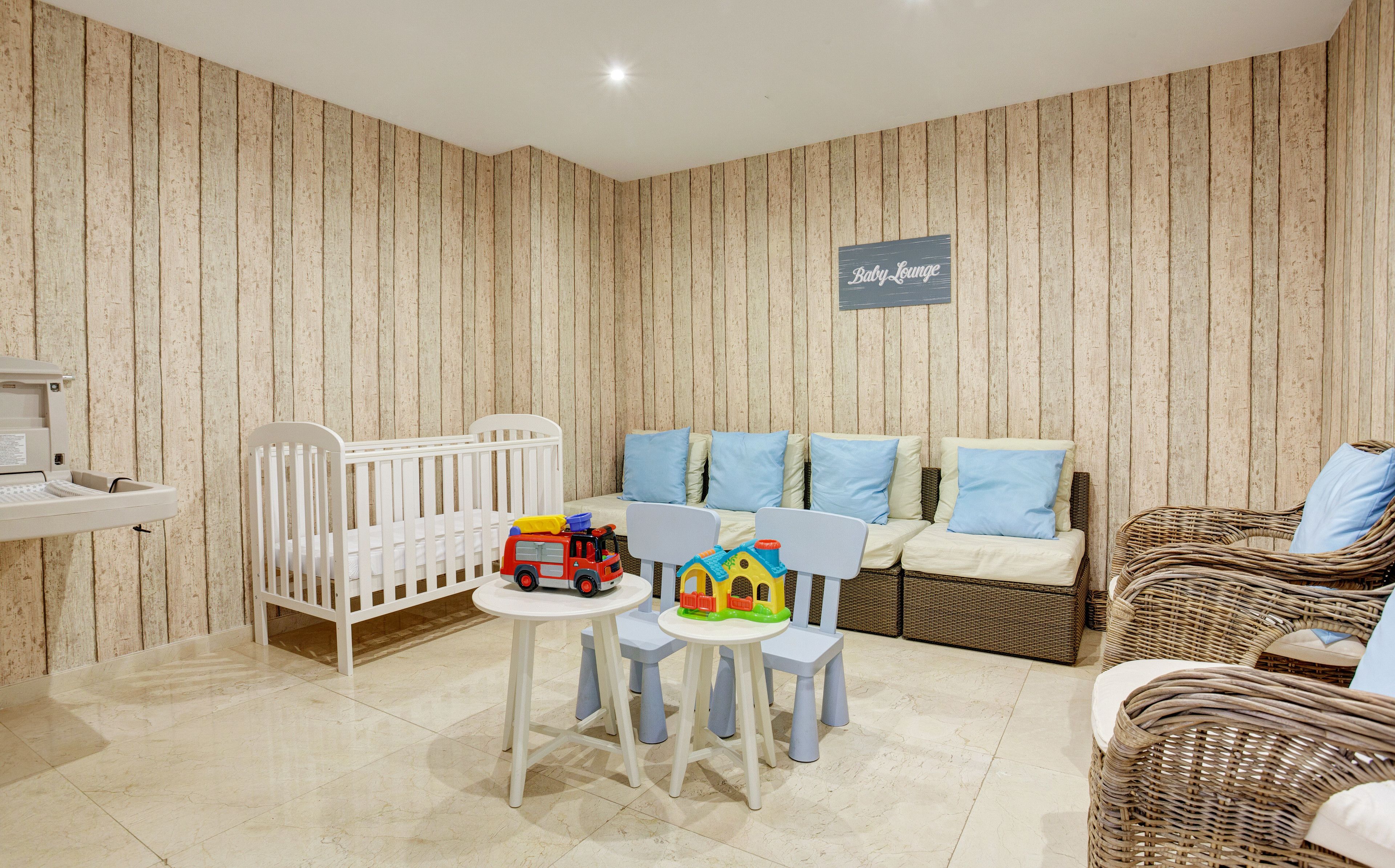A baby lounge with a crib, a play table, and a sofa with blue cushions.