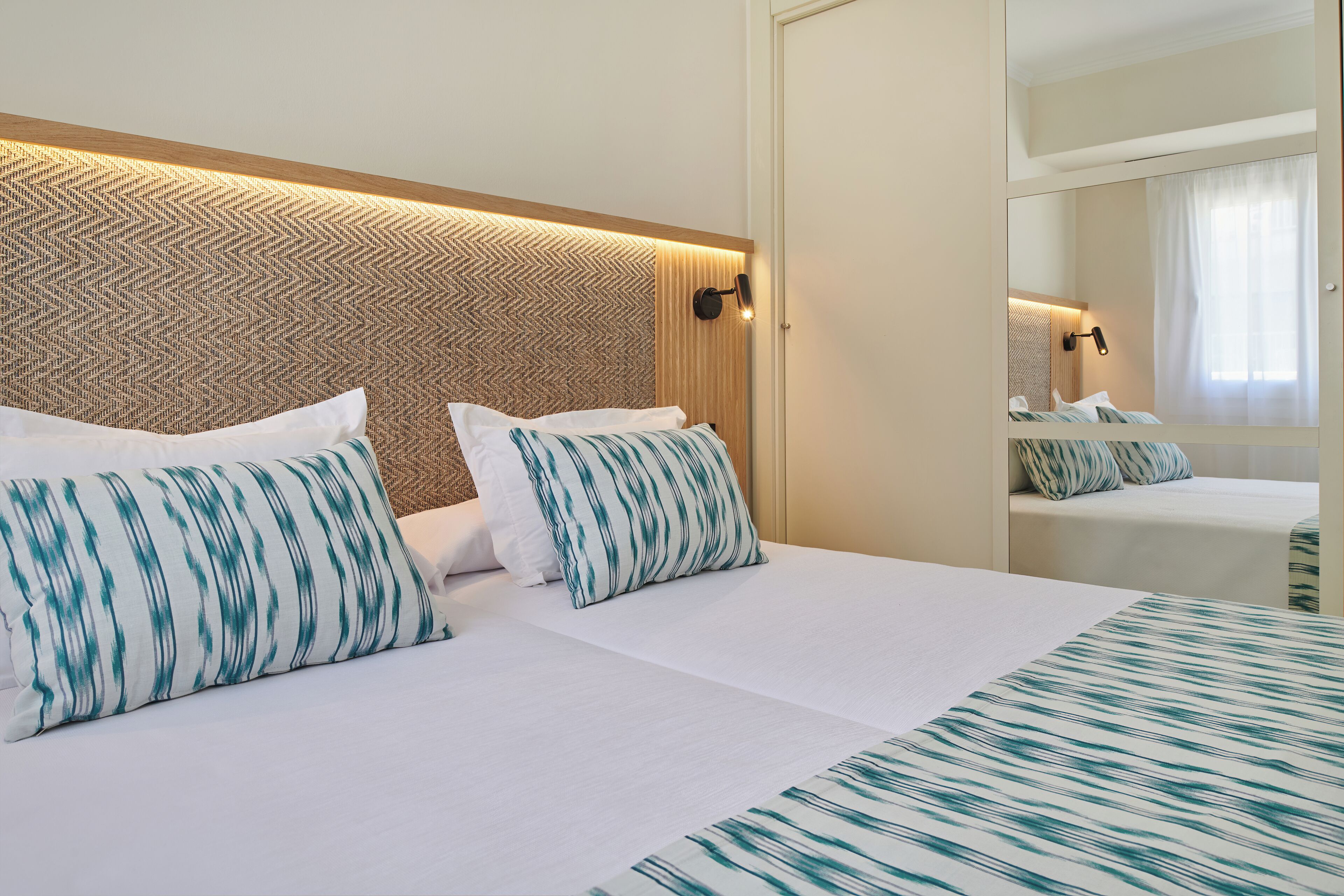 A hotel room with two beds, a large mirror, and a patterned headboard.