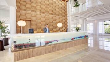 Zona de recepción con pared de madera, mostrador de vidrio y vista al mar.