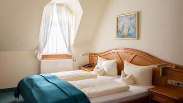 Un dormitorio con una cama de madera, una mesita de noche y una ventana con cortina ligera, además de un cuadro en la pared.