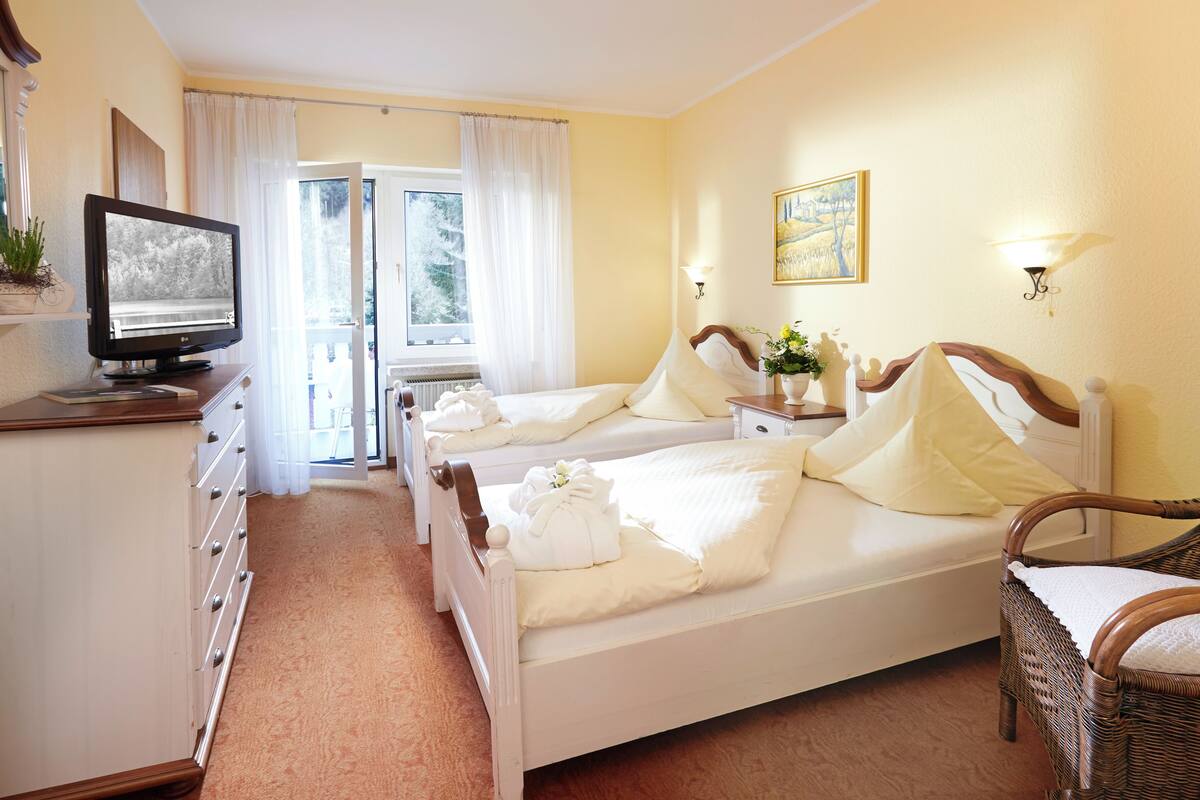 A hotel room with two beds, a television, a dresser, a chair, and a window with curtains.