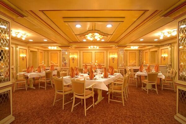Un salón de banquetes con varias mesas dispuestas para comer, con un diseño clásico que incluye candelabros y decoraciones ornamentales en las paredes.