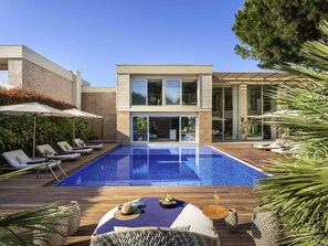 A modern house with a swimming pool, lounge chairs, and a dining area with outdoor furniture.