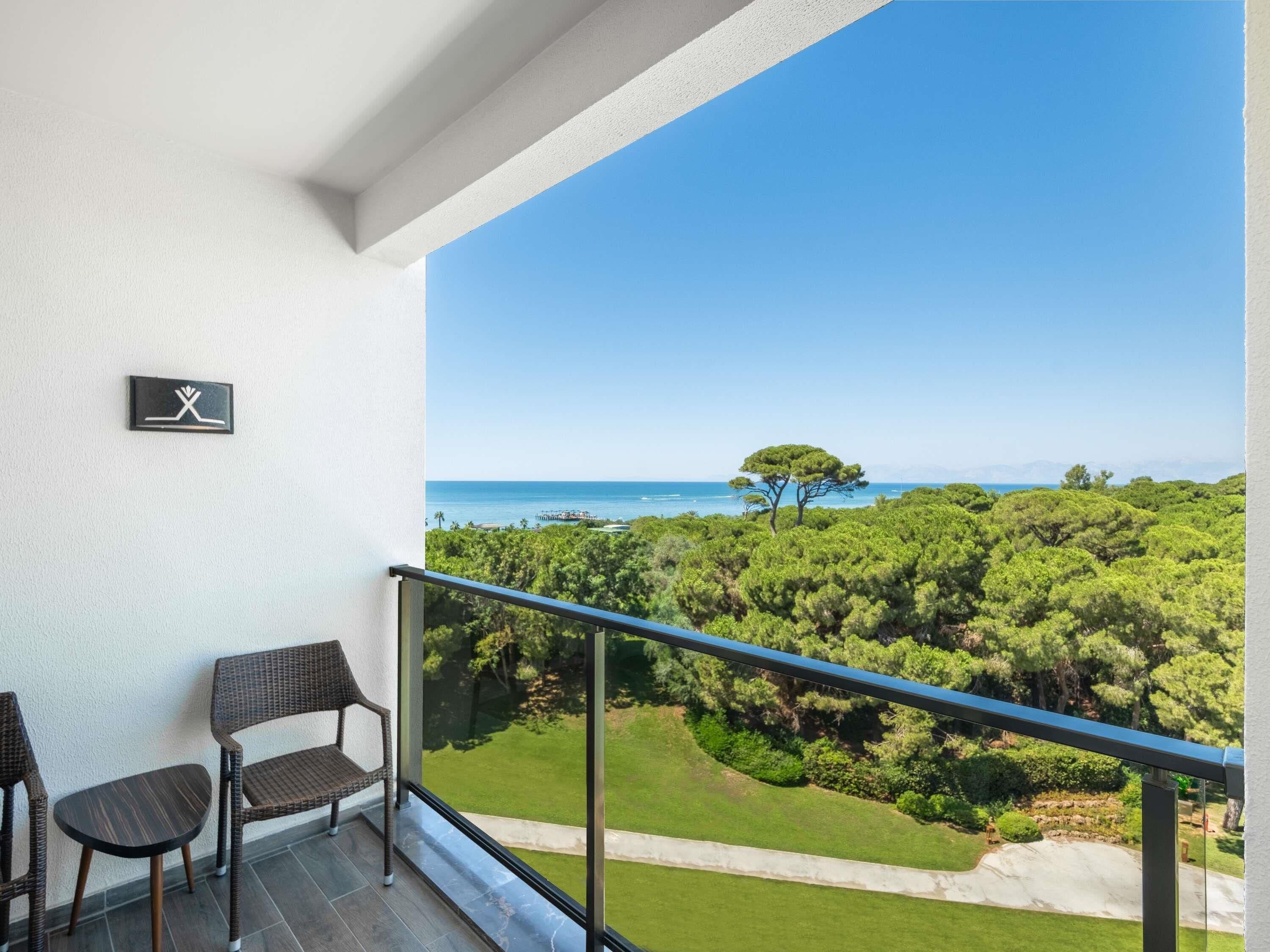 Ein Balkon mit Blick auf das Meer und einen Baum, ausgestattet mit zwei Stühlen und einem kleinen Tisch.