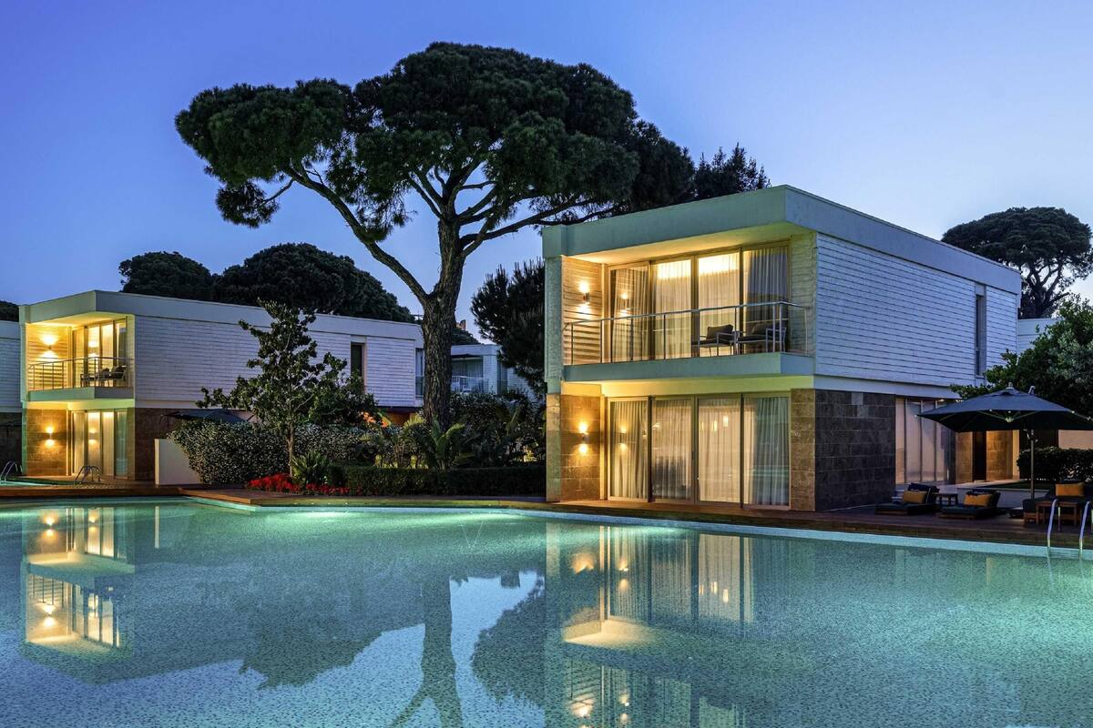 A modern two-story house with a swimming pool, large windows, and outdoor seating.