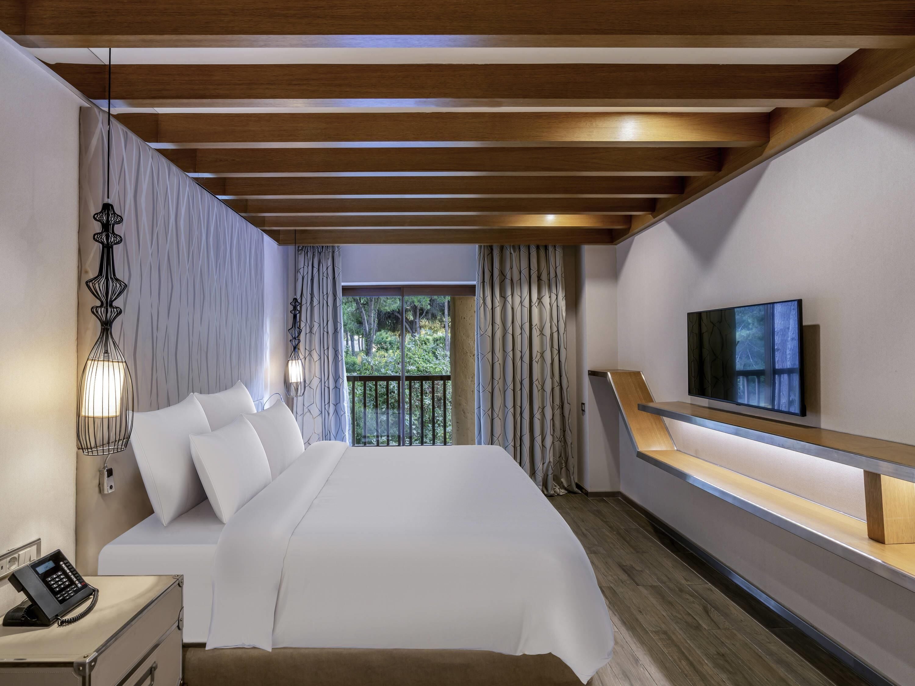 A modern bedroom with a bed, bedside table, lamp, TV, and a balcony with curtains.