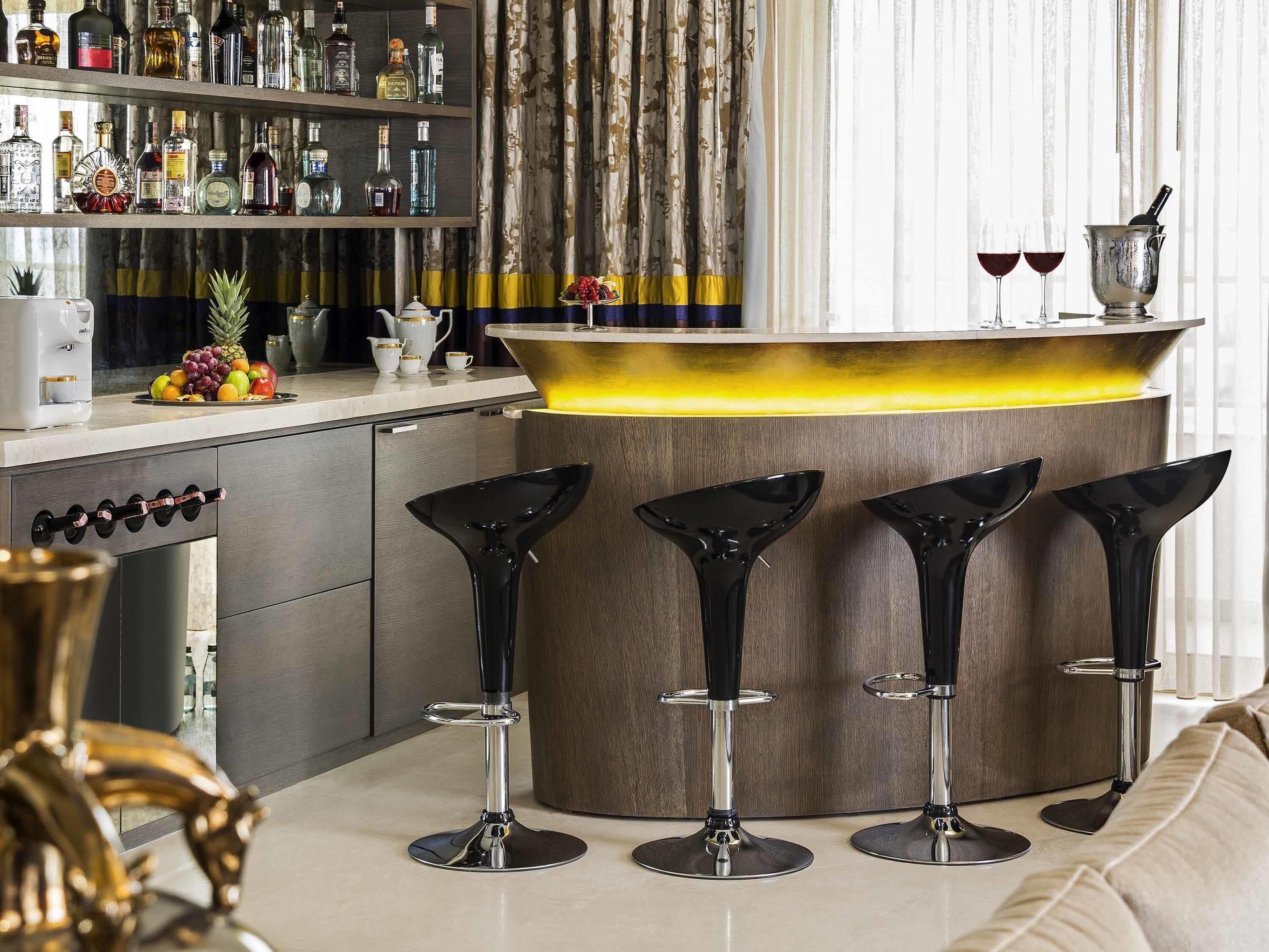 A bar area with a countertop, bar stools, and a wine glass holder.