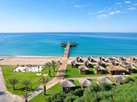 A resort with thatched-roof huts, a beach, and a pier extending into the sea.