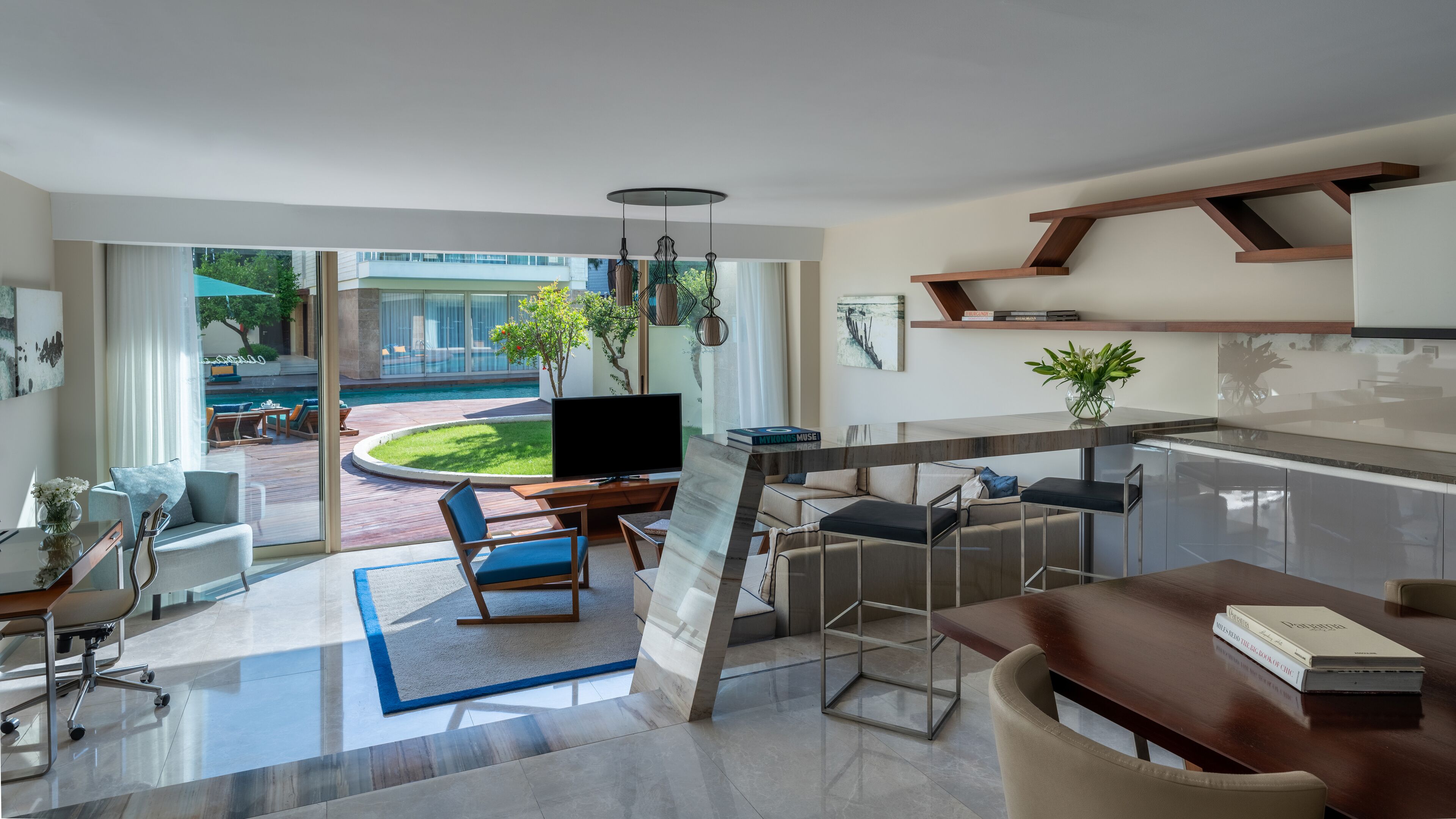 Ein modernes Wohnzimmer mit Fernseher, Sitzgelegenheit und Blick auf einen Swimmingpool.