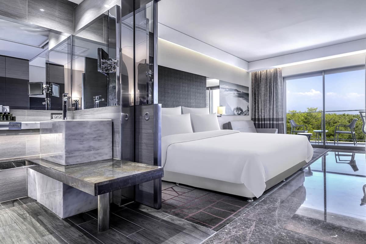 A modern hotel room with a large bed, a glass-enclosed balcony, and a sleek bathroom.