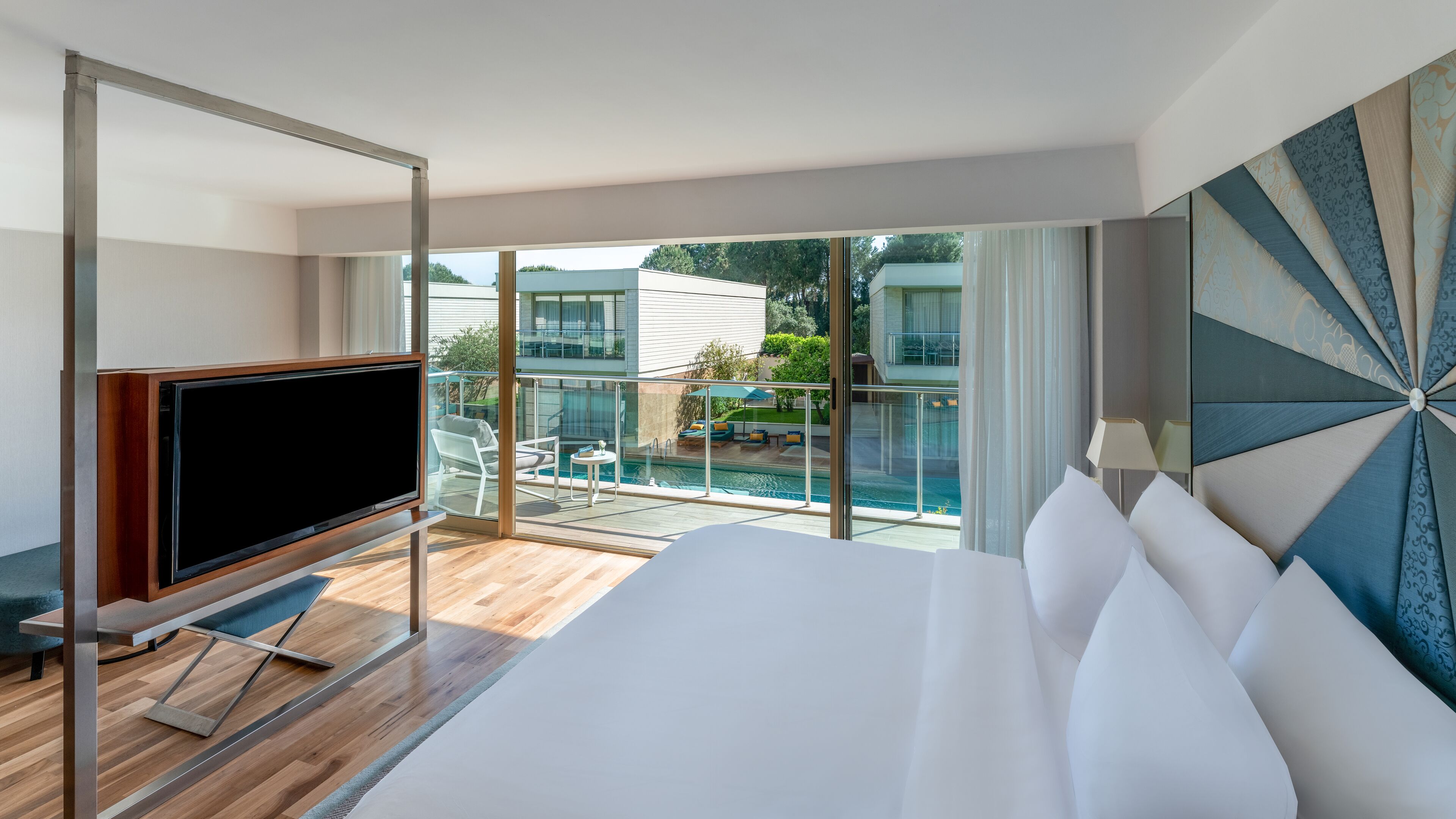 A modern hotel room with a large bed, a flat-screen TV, and a balcony with a pool.