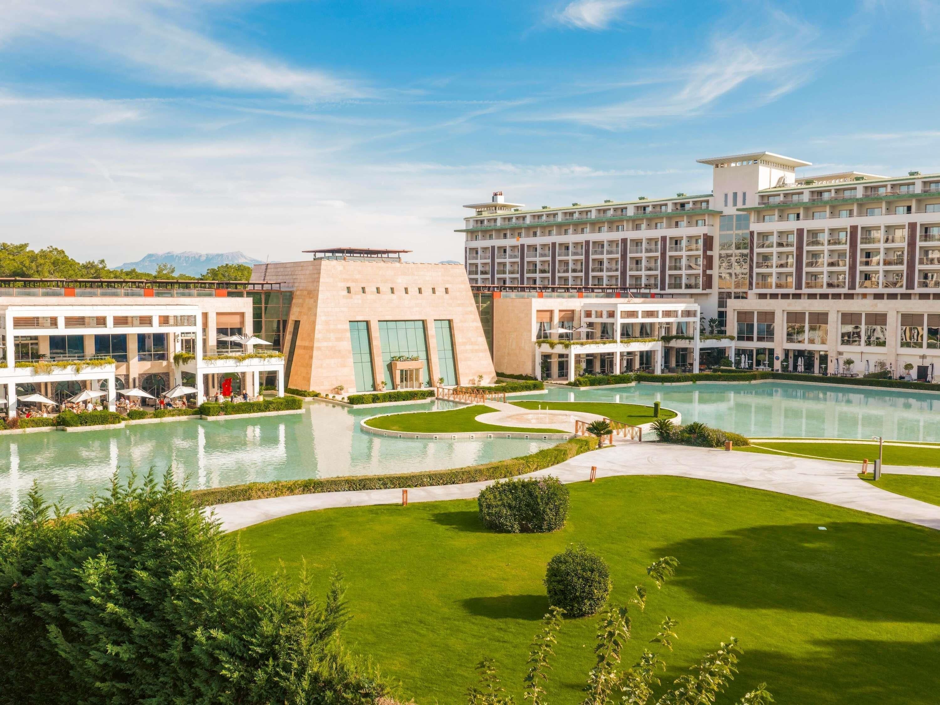 A hotel with multiple swimming pools, a well-maintained lawn, and a large building with a modern design.