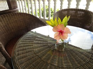 A round glass table with a woven wicker chair on a balcony. - Lazare Picault Hotel (Mahé Island)