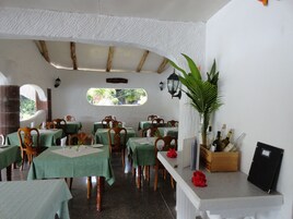 Un restaurante con manteles verdes, sillas de madera y una planta grande en maceta.