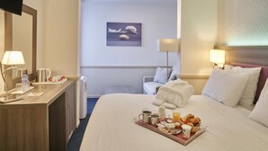 Habitación de hotel con cama, mesita de noche, lámpara y una bandeja con artículos de desayuno.