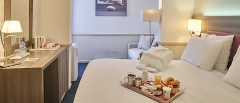 A hotel room with a bed, bedside table, lamp, and a tray of breakfast items.