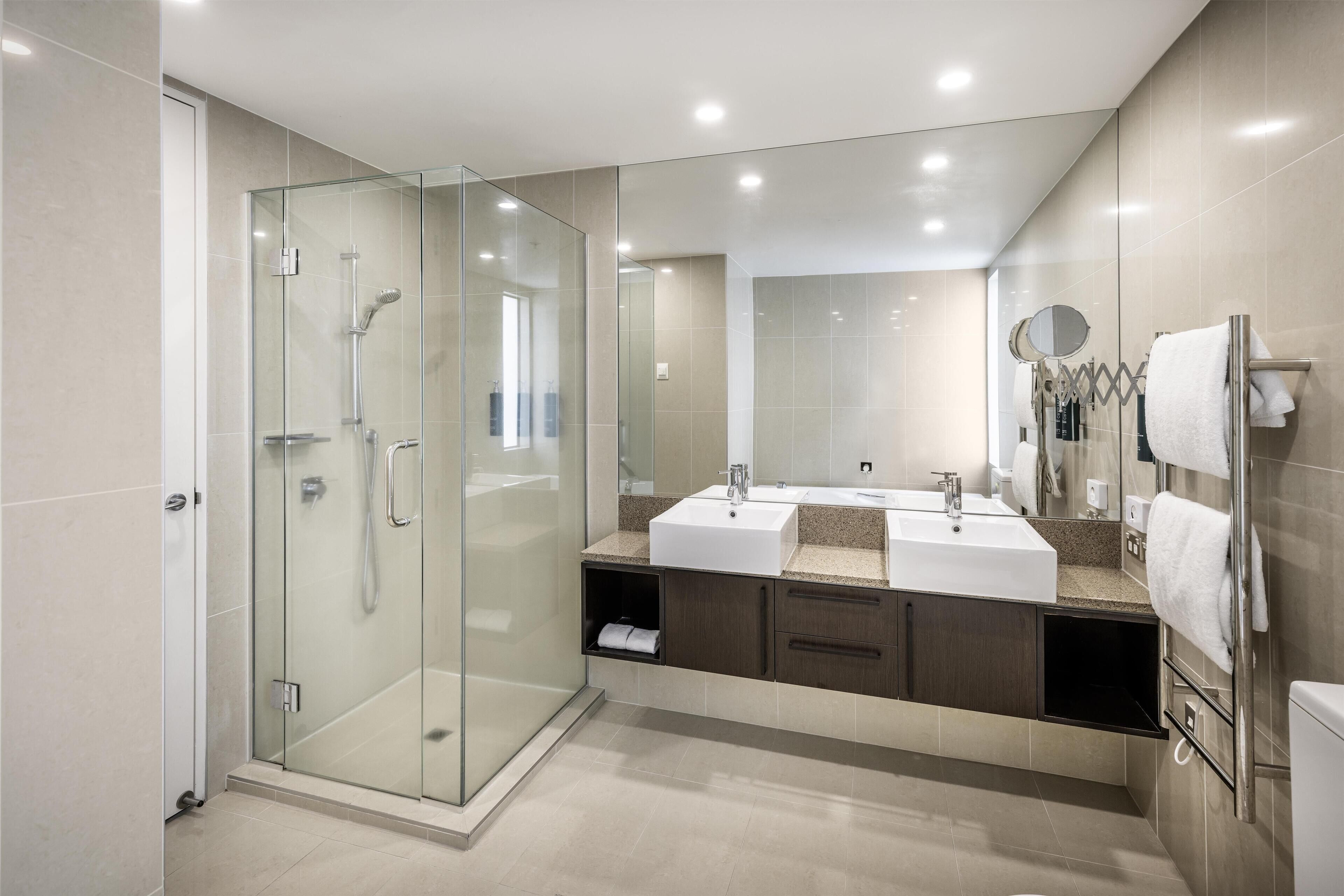 A modern bathroom with a glass-enclosed shower, dual sinks, and a large mirror.