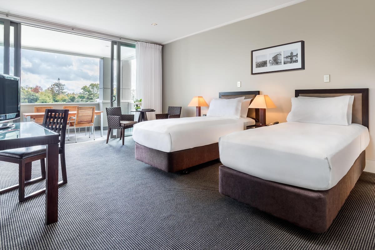 Une chambre d’hôtel avec deux lits, un bureau, des chaises, une télévision et un balcon avec vue.