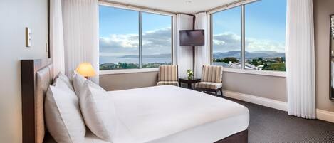 A hotel room with a large bed, a TV, two chairs, and a view of the landscape.